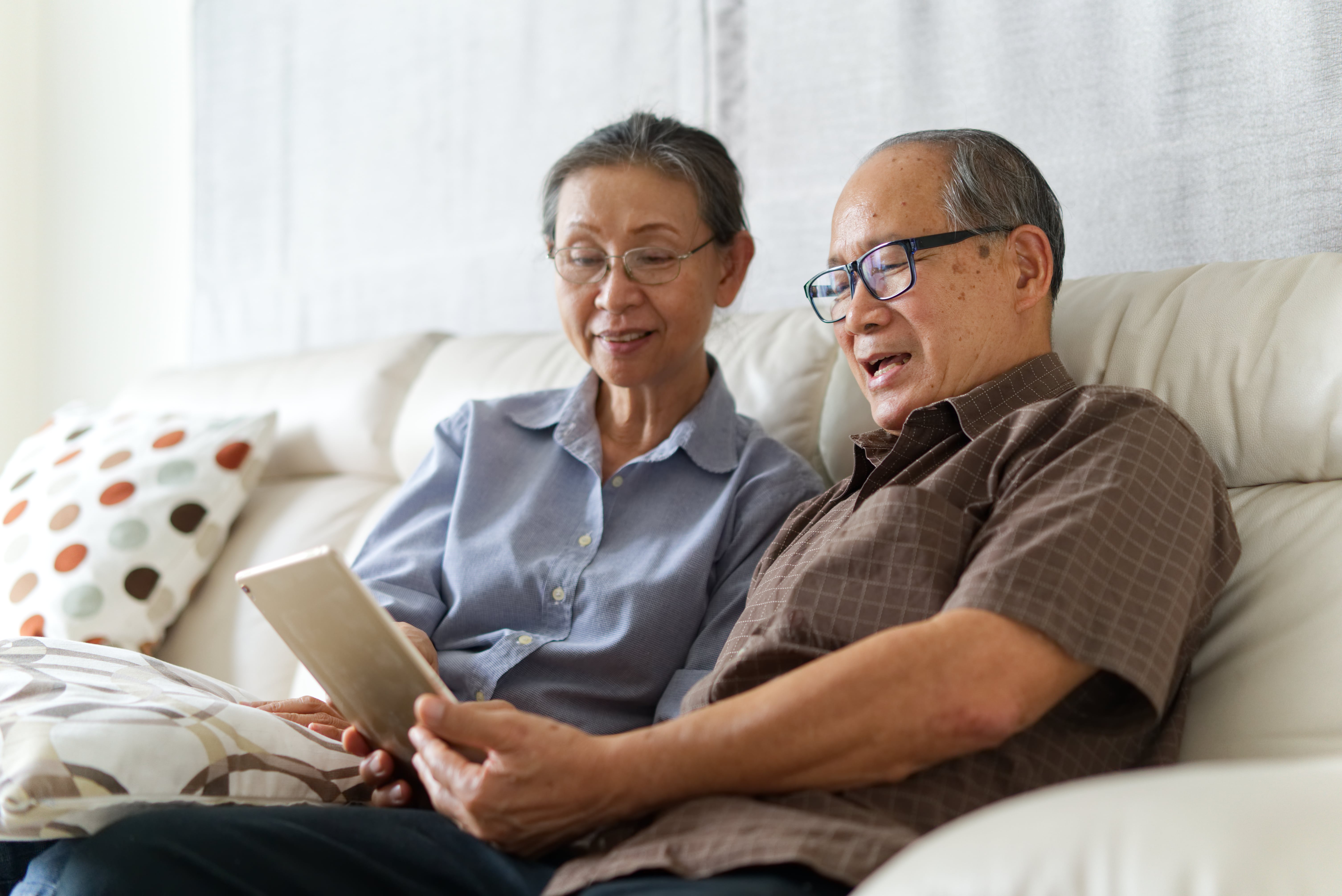happy couple sitting on sofa looking at tablet