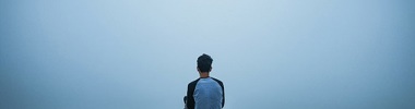 boy sitting on hill looking out into a misty landscape