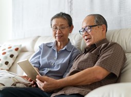 happy couple sitting on sofa looking at tablet