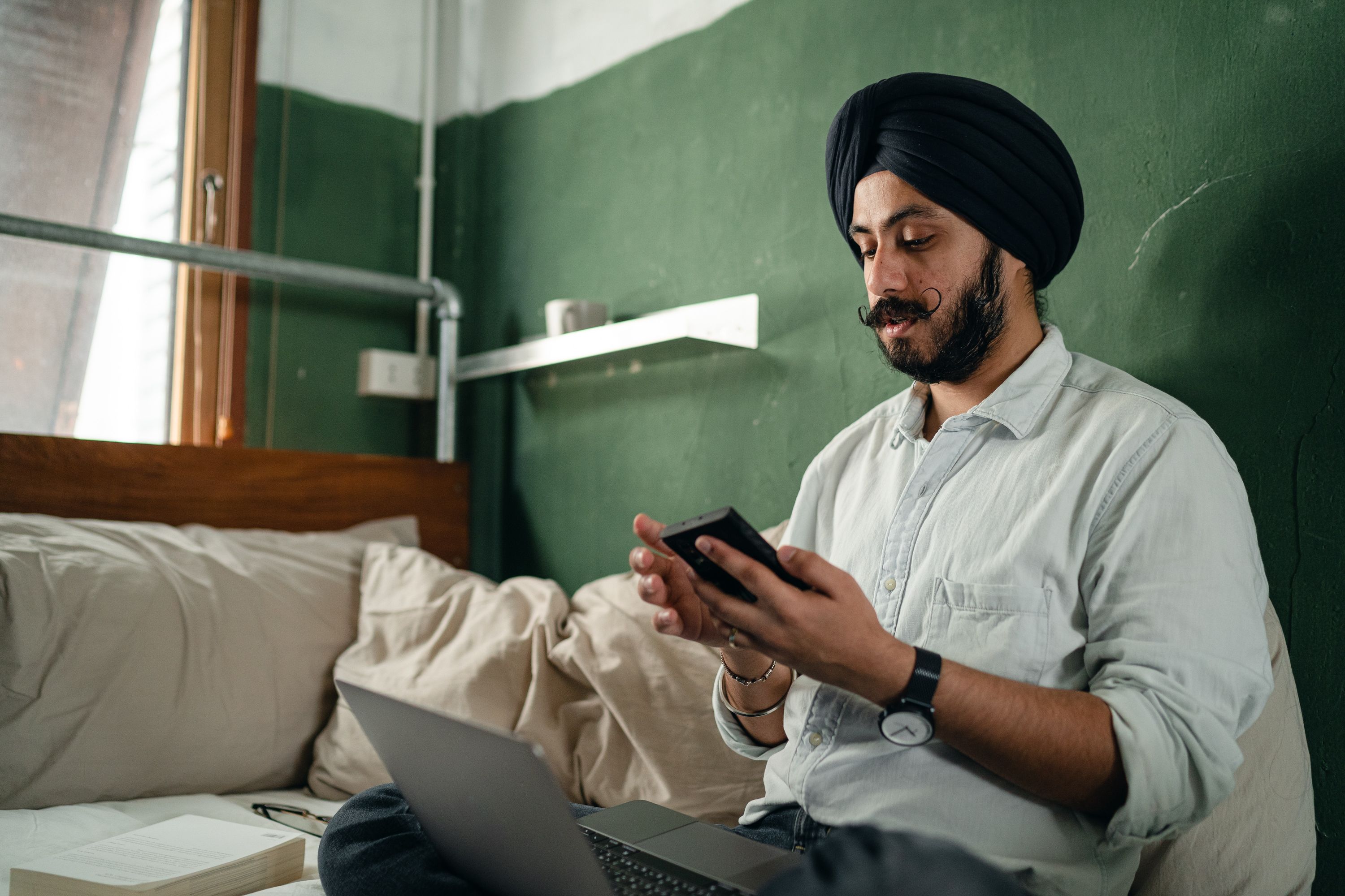 Sikh man sitting on bed using phone