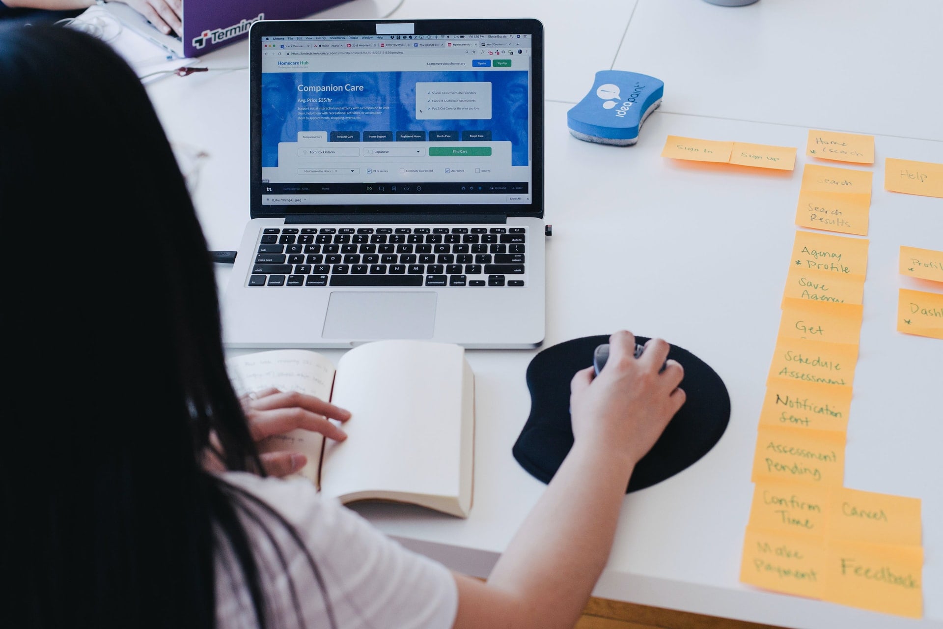 Woman using computer at a table next to a column of post it notes