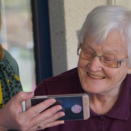 care worker wearing mask shows older woman a smartphone