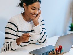 Smiling woman looking at computer with a cup of tea