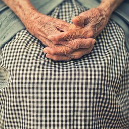 older woman with hands clasped on lap