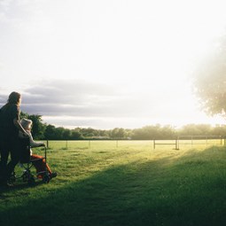 woman pushing person in wheelchair across a field
