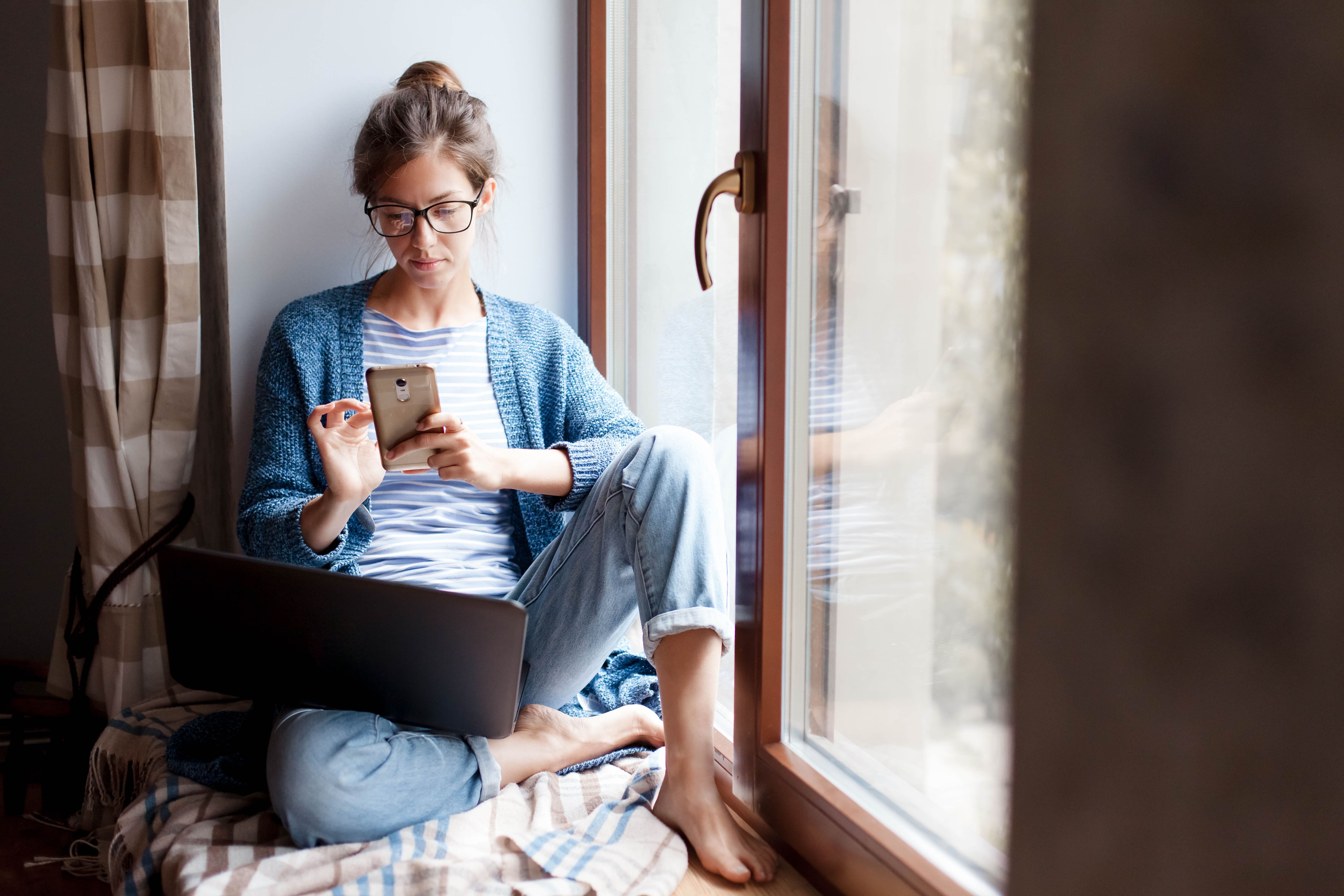 Woman carer sits in windowsill looking at a smartphone