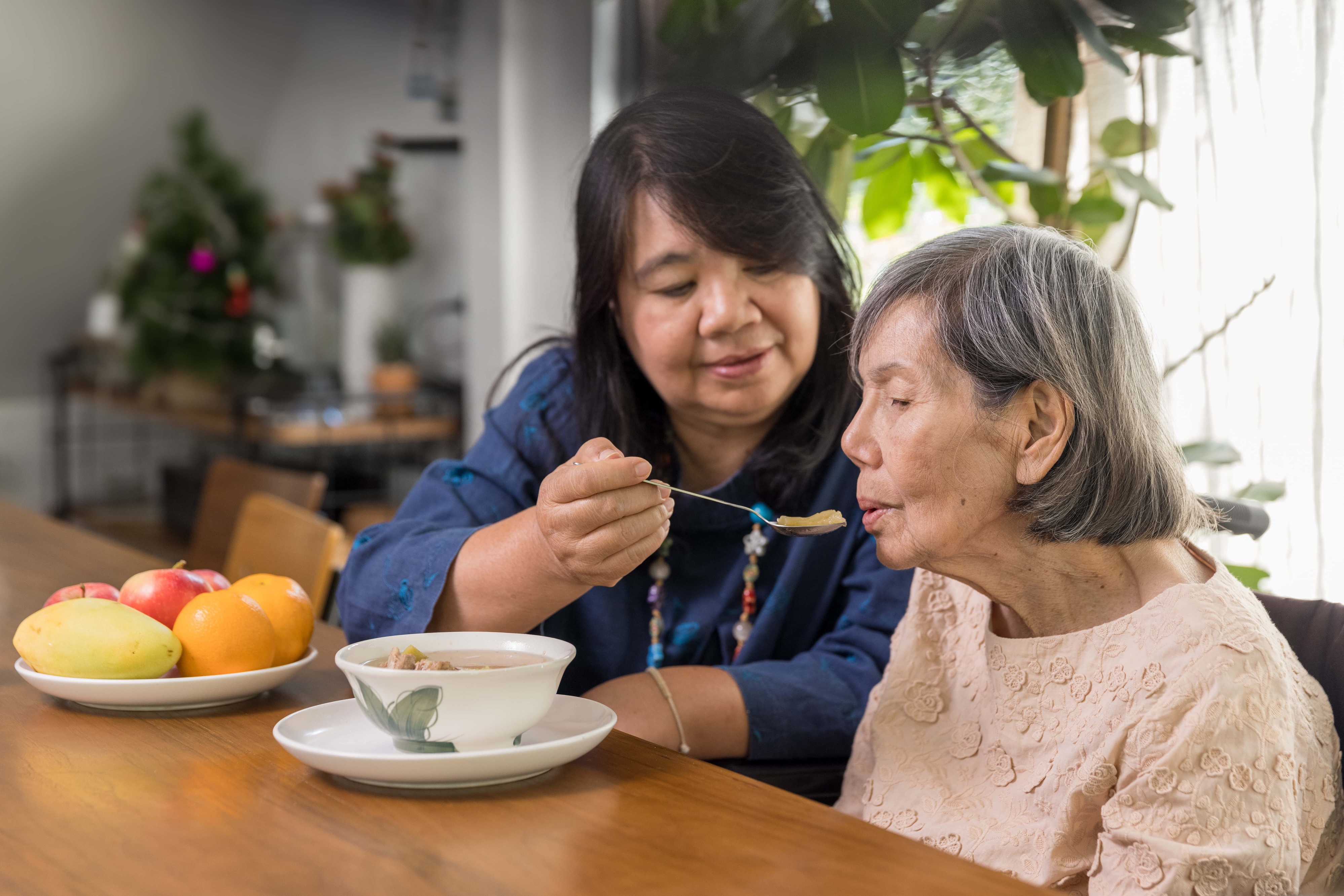 woman helping older woman eat in a kitchen
