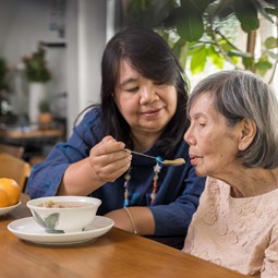 woman helping older woman eat in a kitchen